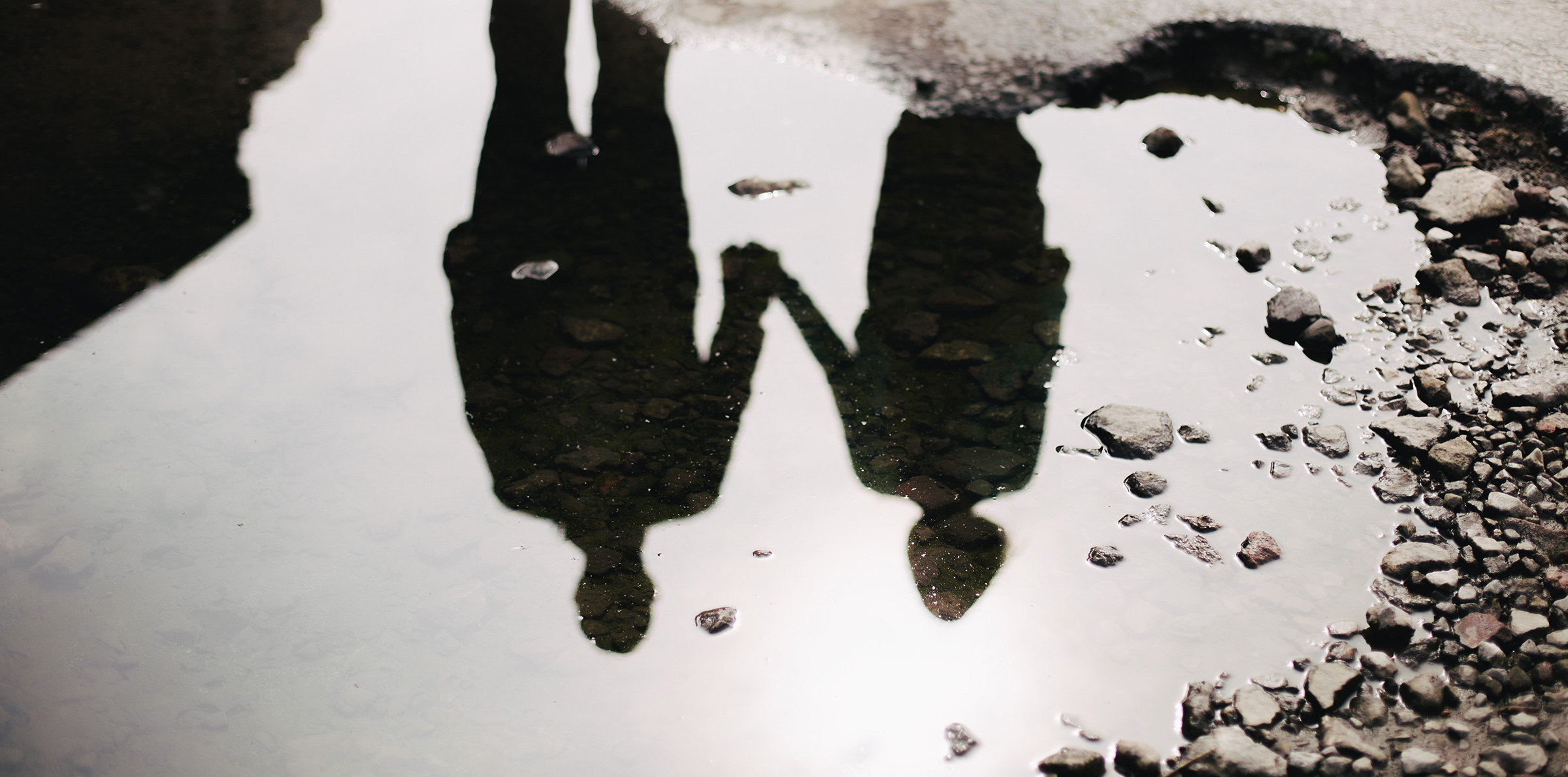 puddle reflection of introspective couple holding hands
