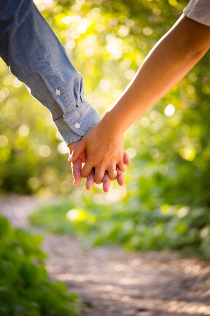A married couple's hands holding each other on a nature trail.