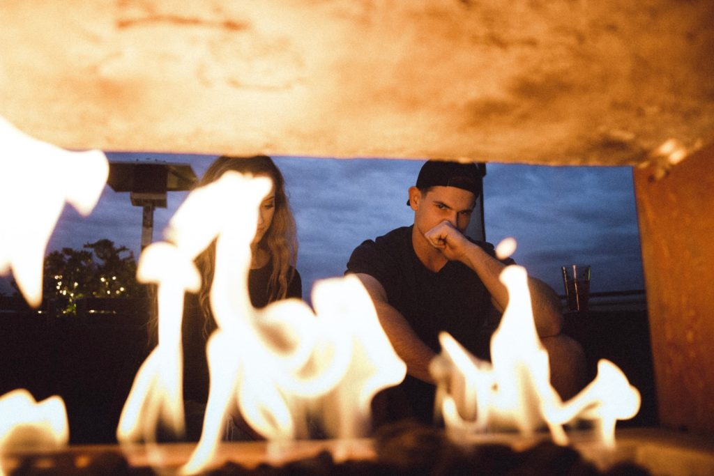 A fire from a fireplace blocks the face of a woman, as the man sitting next to her stares into the fire.