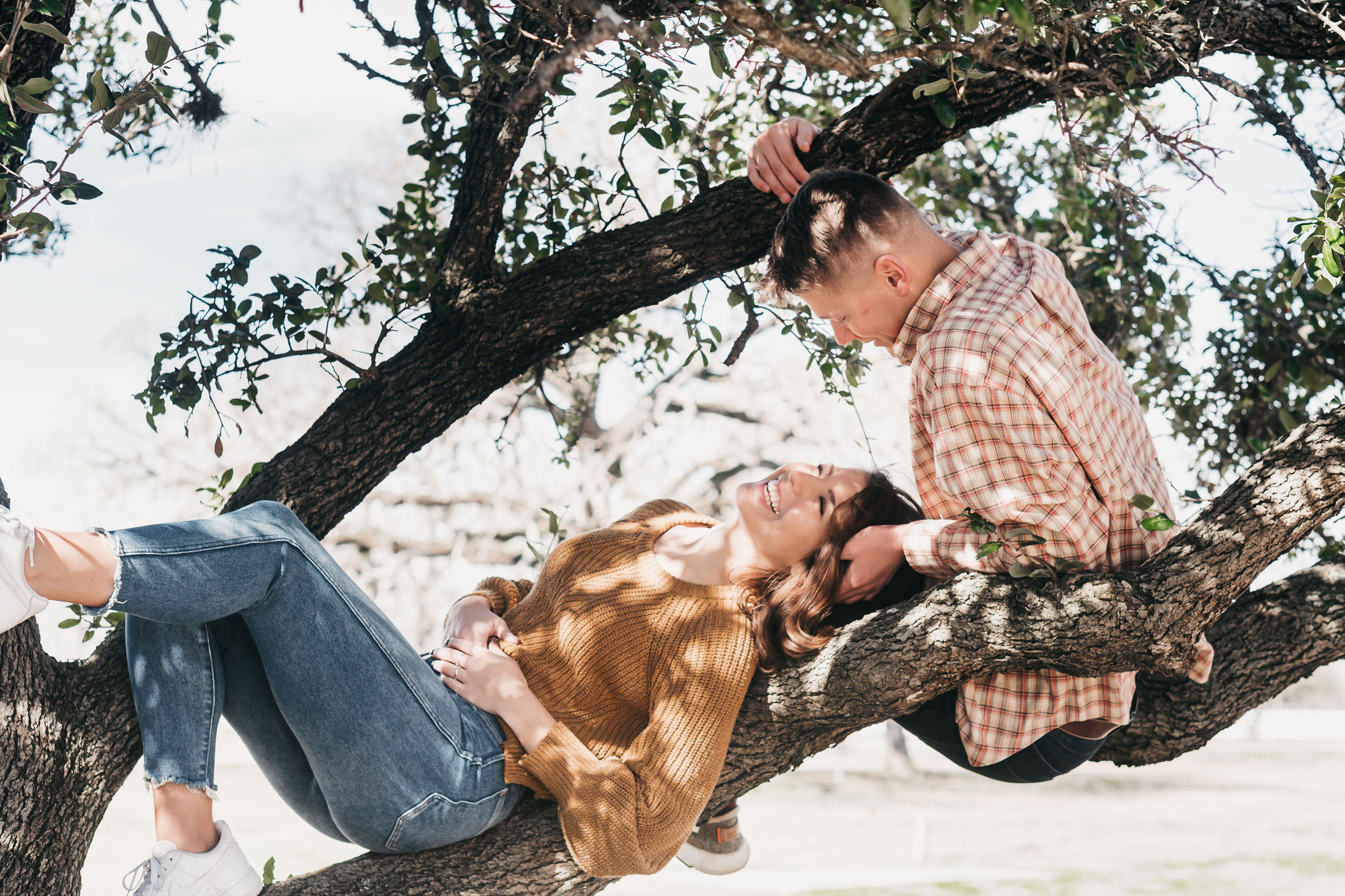 A happy smiling couple lay on a tree branch.