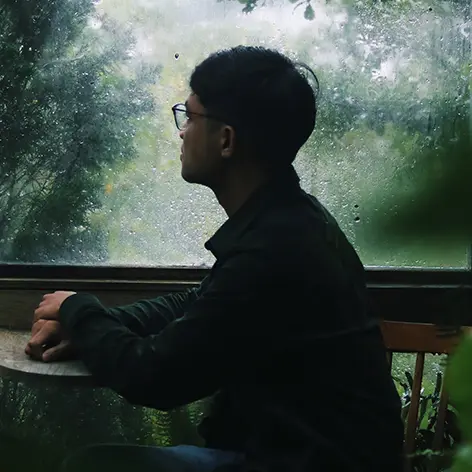 A man sits at a table, looking out at greenery behind a rainy window—can he be helped by therapy for depression?
