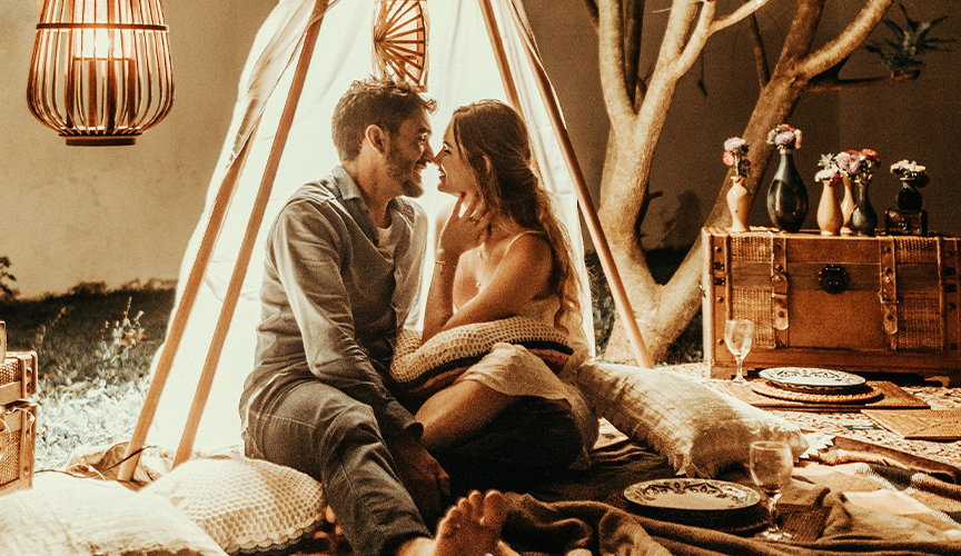 A couple inside a glowing tent, looking into each other's eyes, smiling, and connecting deeply with each other on their honeymoon.