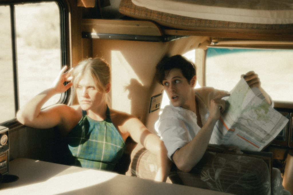 A husband and wife sit in a van during their honeymoon, the man holding a map and looking expectantly at the woman, who is upset.