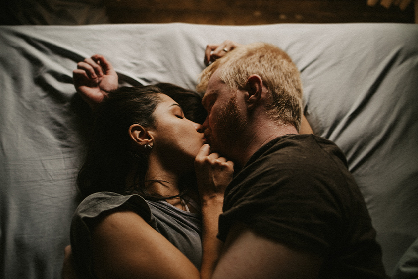 A man and woman lie in bed, gently kissing and comforting each other after their relationship was nearly ruined.
