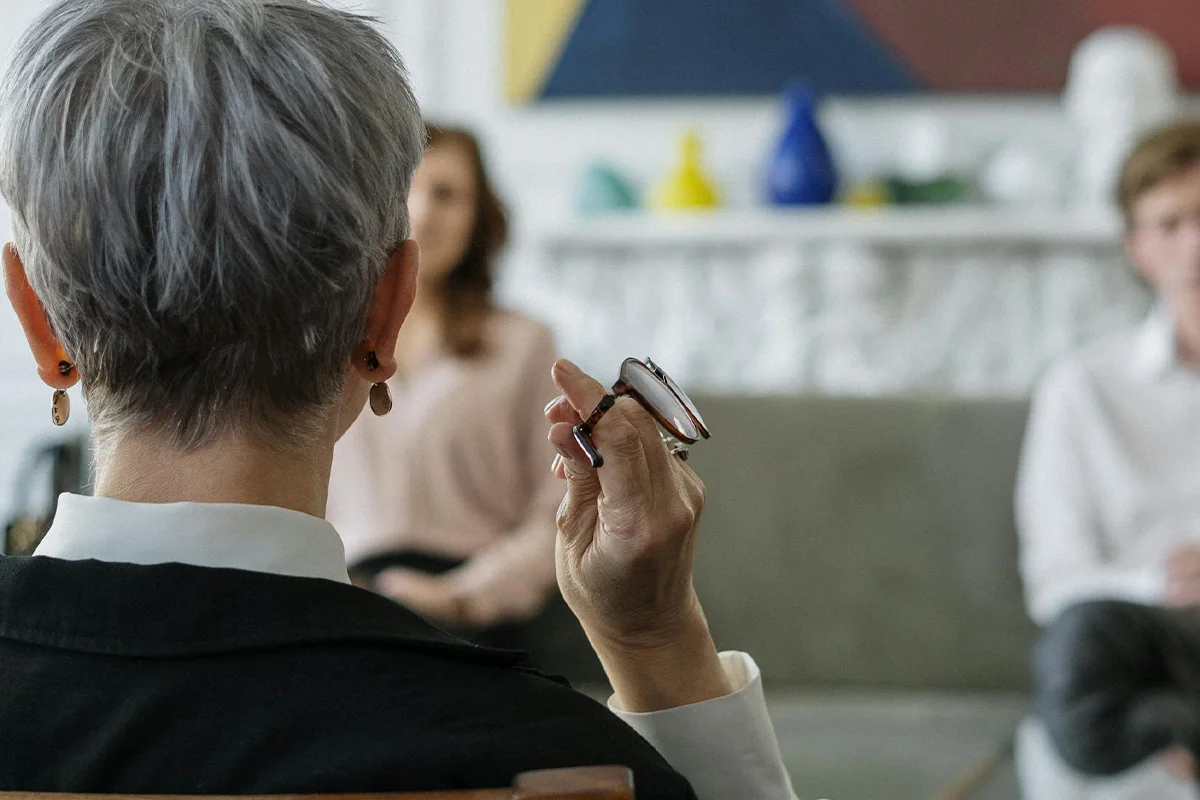 The back of a couples therapist's head in a cold, cool setting, with the couple blurred out and disconnected in the background — this is not the kind of therapist you want to find.