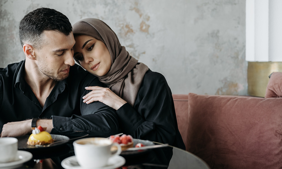 A man and woman are sitting in a restaurant, her hand and head resting on his shoulder. Codependent, overly attached, or human?