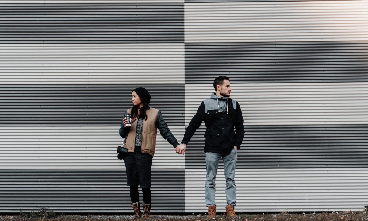 A couple hold hands, facing away from each other as if wanting to connect.