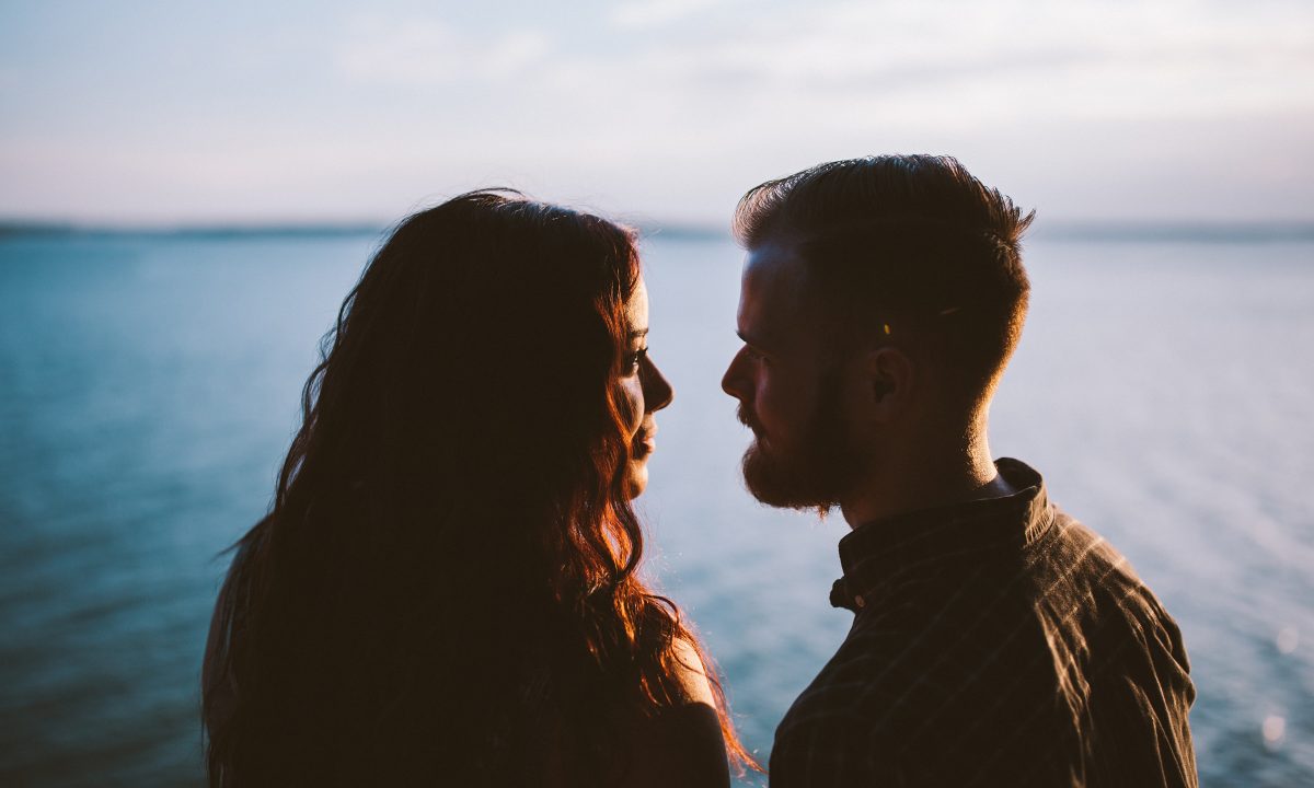 A couple looking at each other in the eyes in front of the ocean.